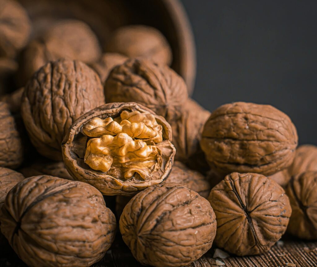 pexels photo 8705561 8705561 Detailed close-up of whole and cracked walnuts in a rustic wooden setting. Ideal for food or nut-themed visuals.